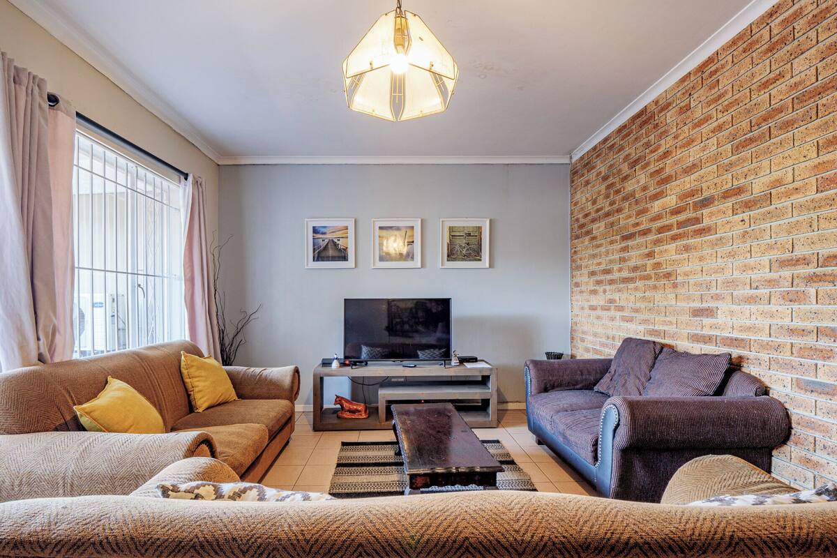 A living room with a brick wall, a television, and two sofas with cushions.