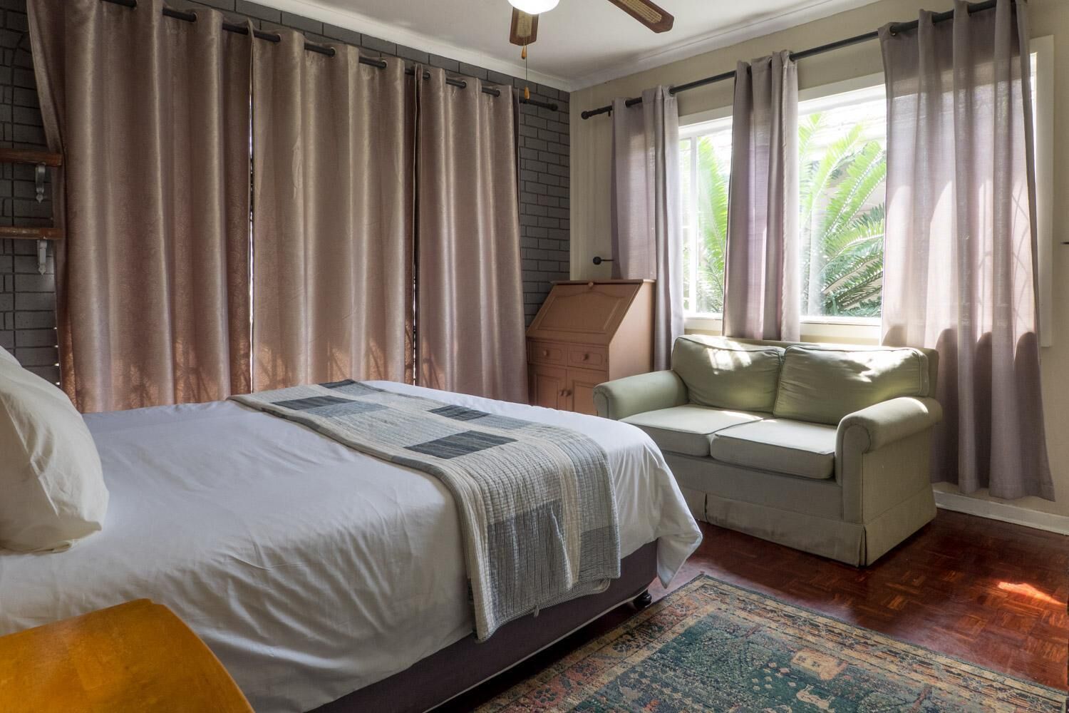 A bedroom with a bed, a sofa, a window with curtains, and a wooden cabinet.