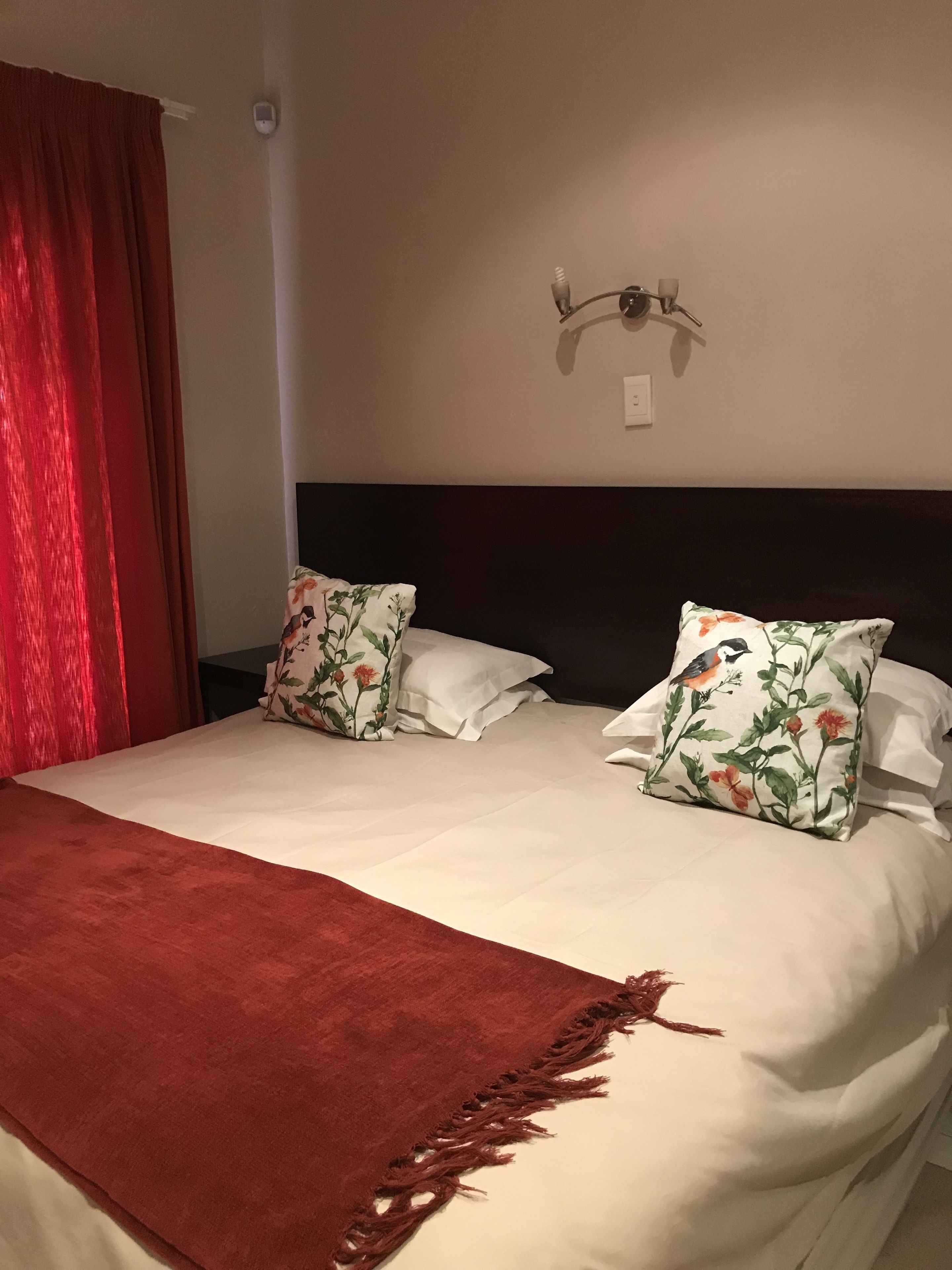A double bed with a red throw blanket, two floral pillows, and a wall-mounted light fixture.