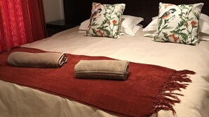 En pænt redt seng med blomsterpuder, et rødt tæppe og et sammenrullet håndklæde.