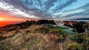 A modern house with a large glass facade, surrounded by natural landscape and a dramatic sky.