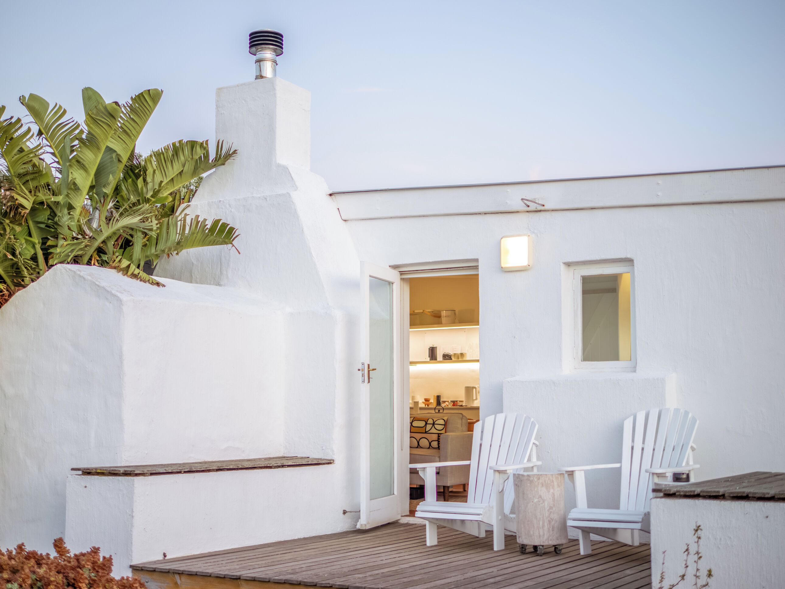 A patio with two white Adirondack chairs, a small round table, and a wooden deck.