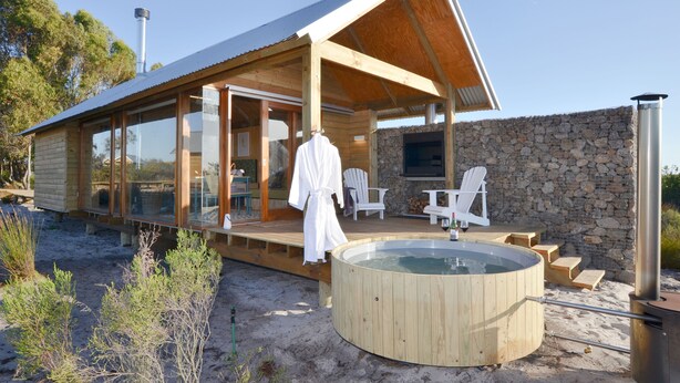 A modern wooden cabin with glass walls, a hot tub, and outdoor seating.