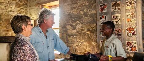 A rustic interior with stone walls, a wooden reception desk, and a bulletin board with various pictures.