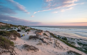 A beach scene with a dune buggy, a small shelter, and a person lying on the sand. - West Coast Luxury Tents- Glamping (Bergrivier)