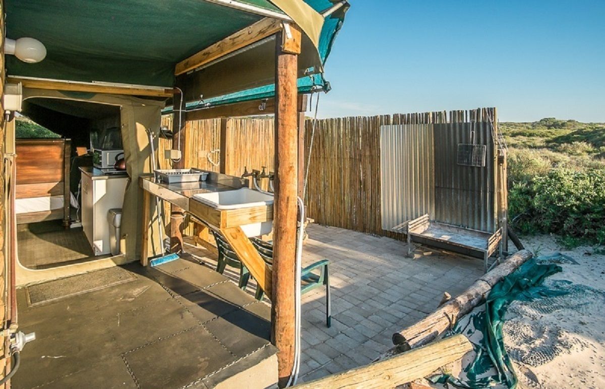 A rustic outdoor kitchen area with a sink and cooking equipment, wooden deck, and a view of the surrounding landscape.
