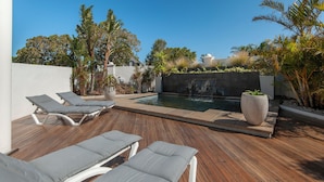 Um deck de madeira com espreguiçadeiras, uma piscina pequena e plantas tropicais.