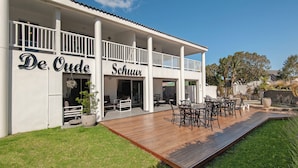 Um edifício de dois andares com um pátio coberto, com deck de madeira e mobiliário para área externa.