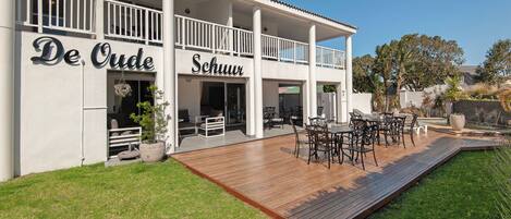 A two-story building with a covered outdoor patio area featuring a wooden deck and outdoor furniture.