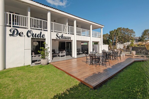 A two-story building with a covered outdoor patio area featuring a wooden deck and outdoor furniture. - Oude Schuur Boutique (Hermanus)