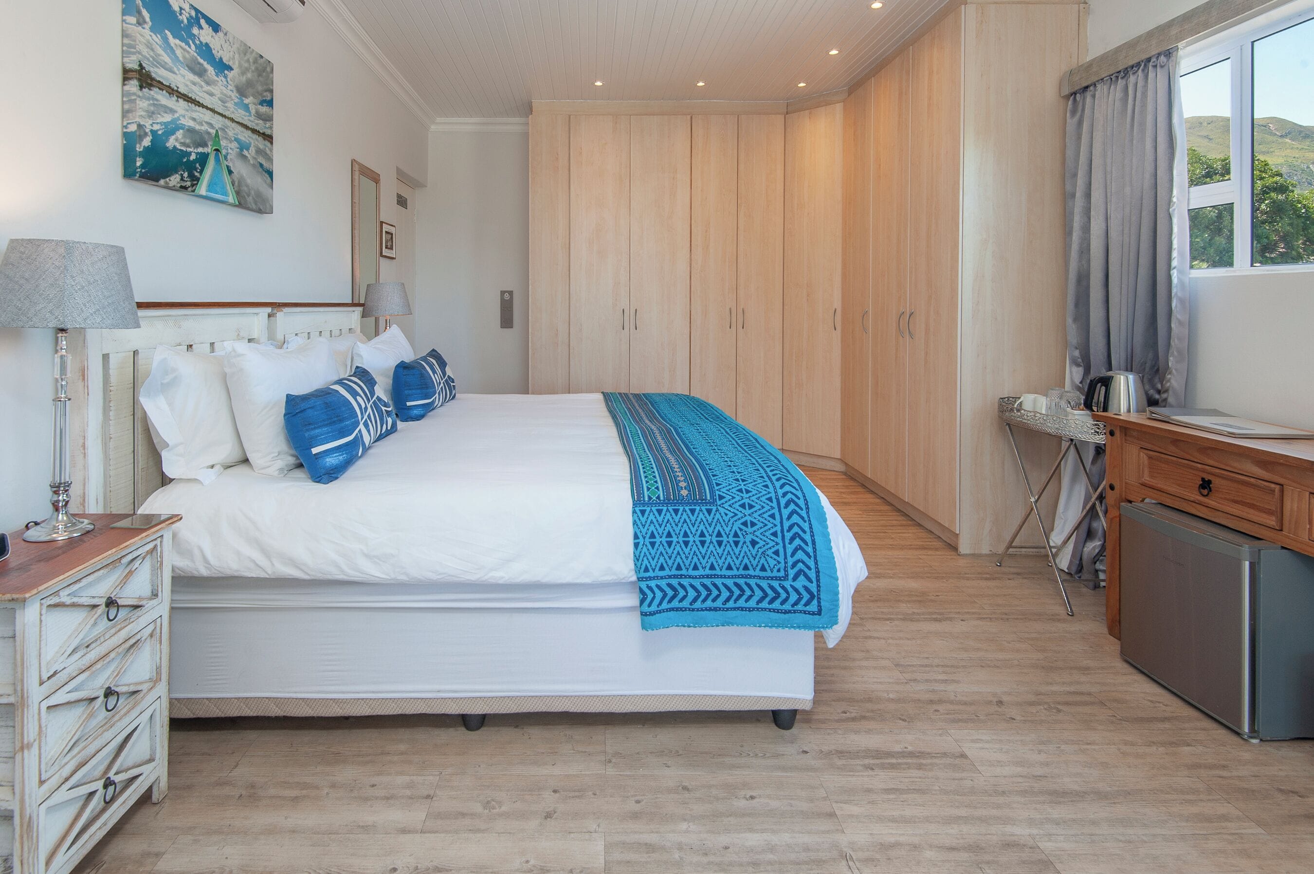 A bedroom with a bed, bedside tables, a wardrobe, a desk with a kettle, and a window with curtains.
