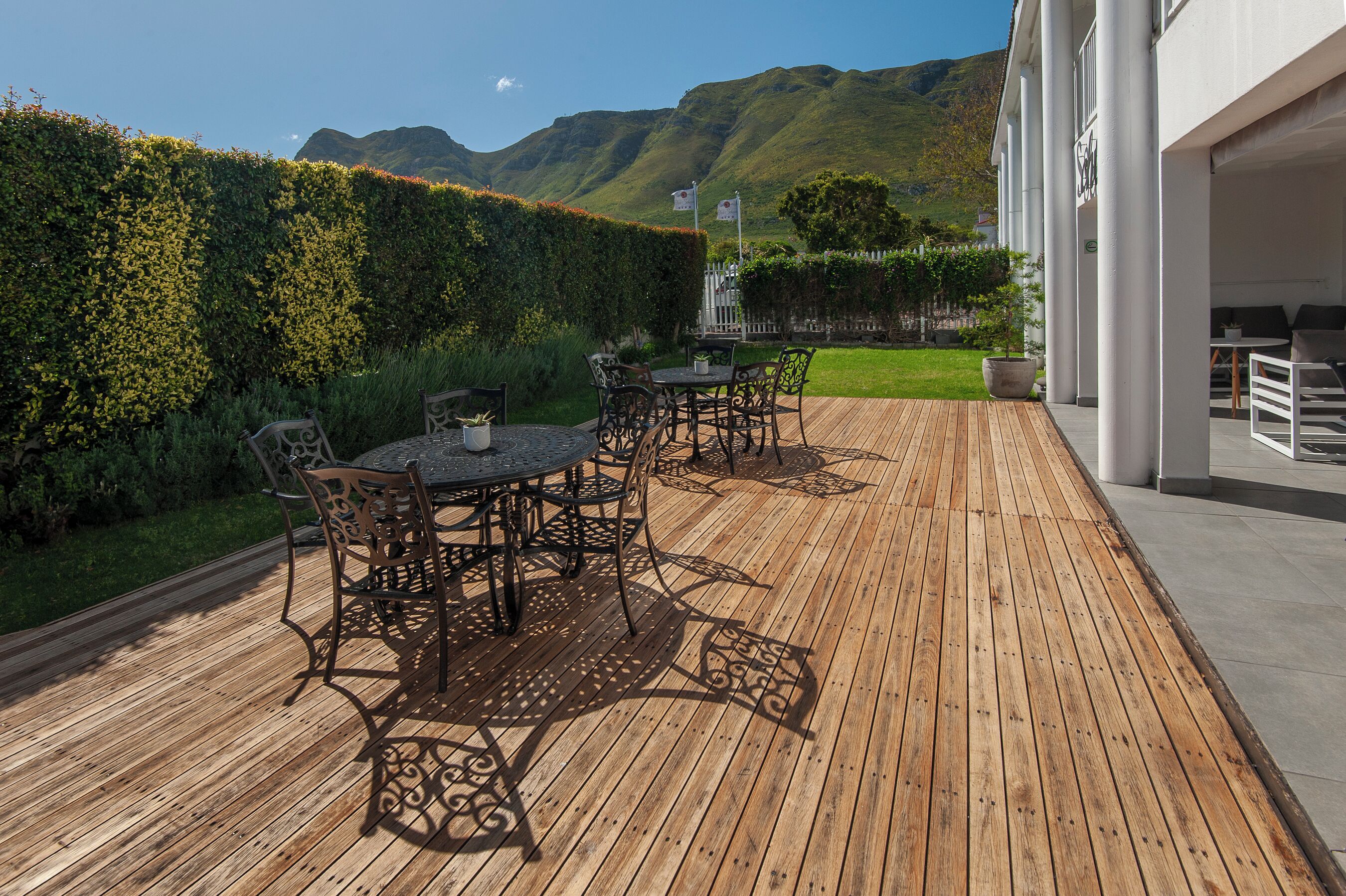 A wooden deck with outdoor seating, a hedge, and a mountain backdrop.