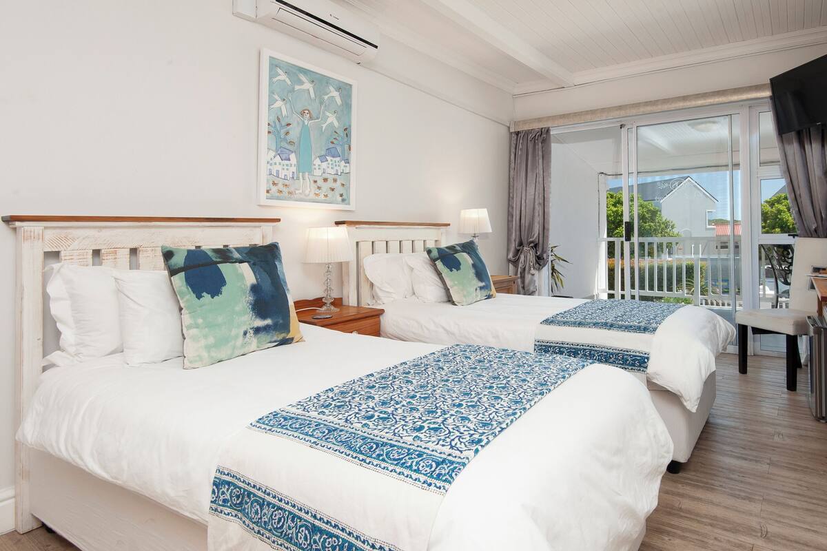A hotel room with two beds, a balcony, and a painting on the wall.