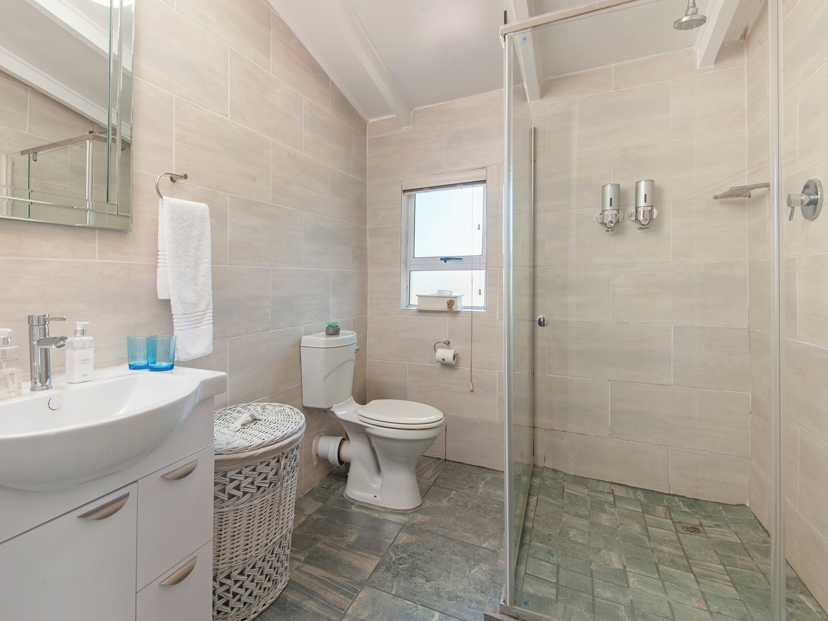 A modern bathroom with a glass-enclosed shower, a sink with toiletries, and a toilet.