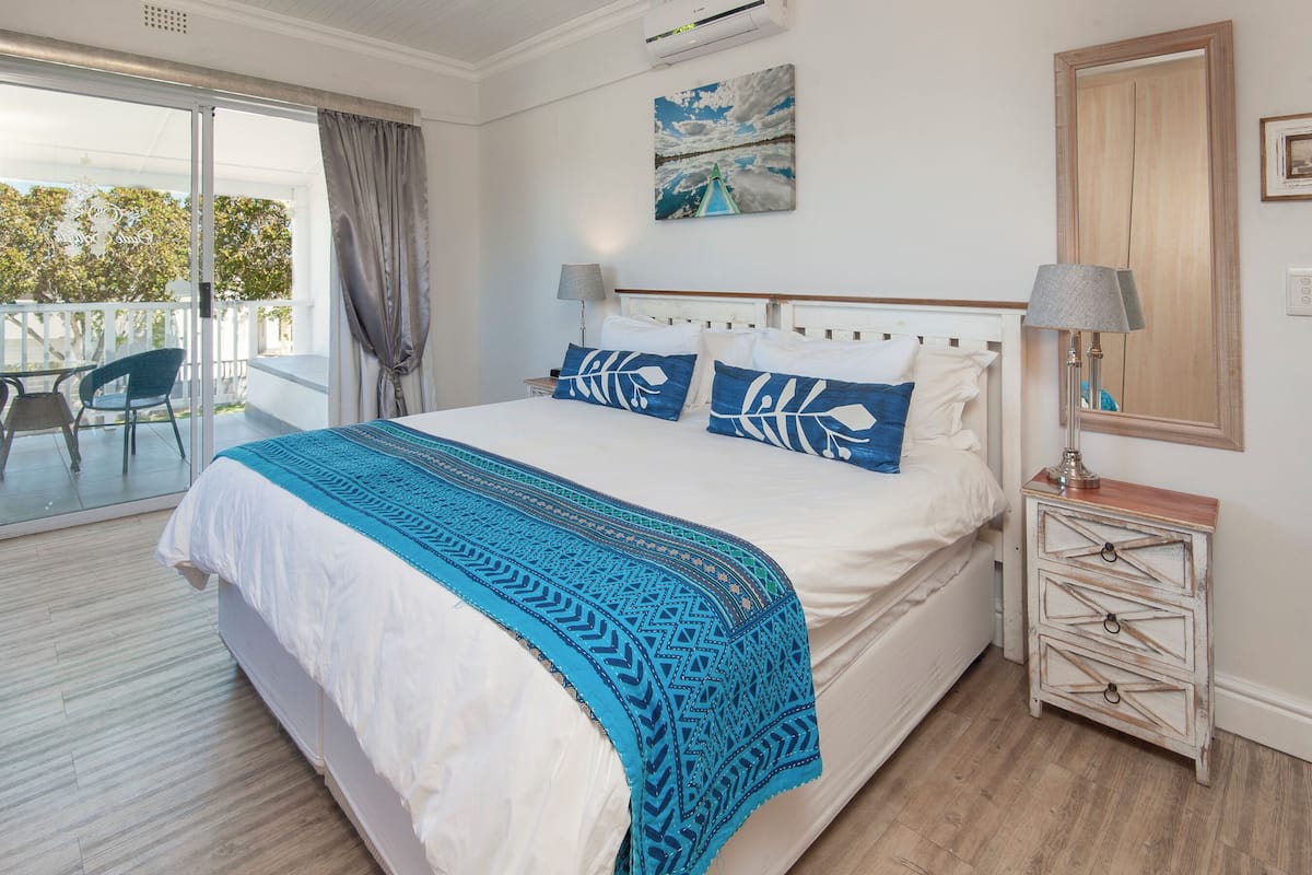 A bedroom with a large bed, a nightstand, a lamp, and a view of the outdoors.