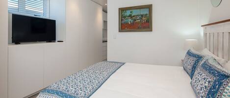 A bedroom with a bed, a TV, a painting, and a lamp.