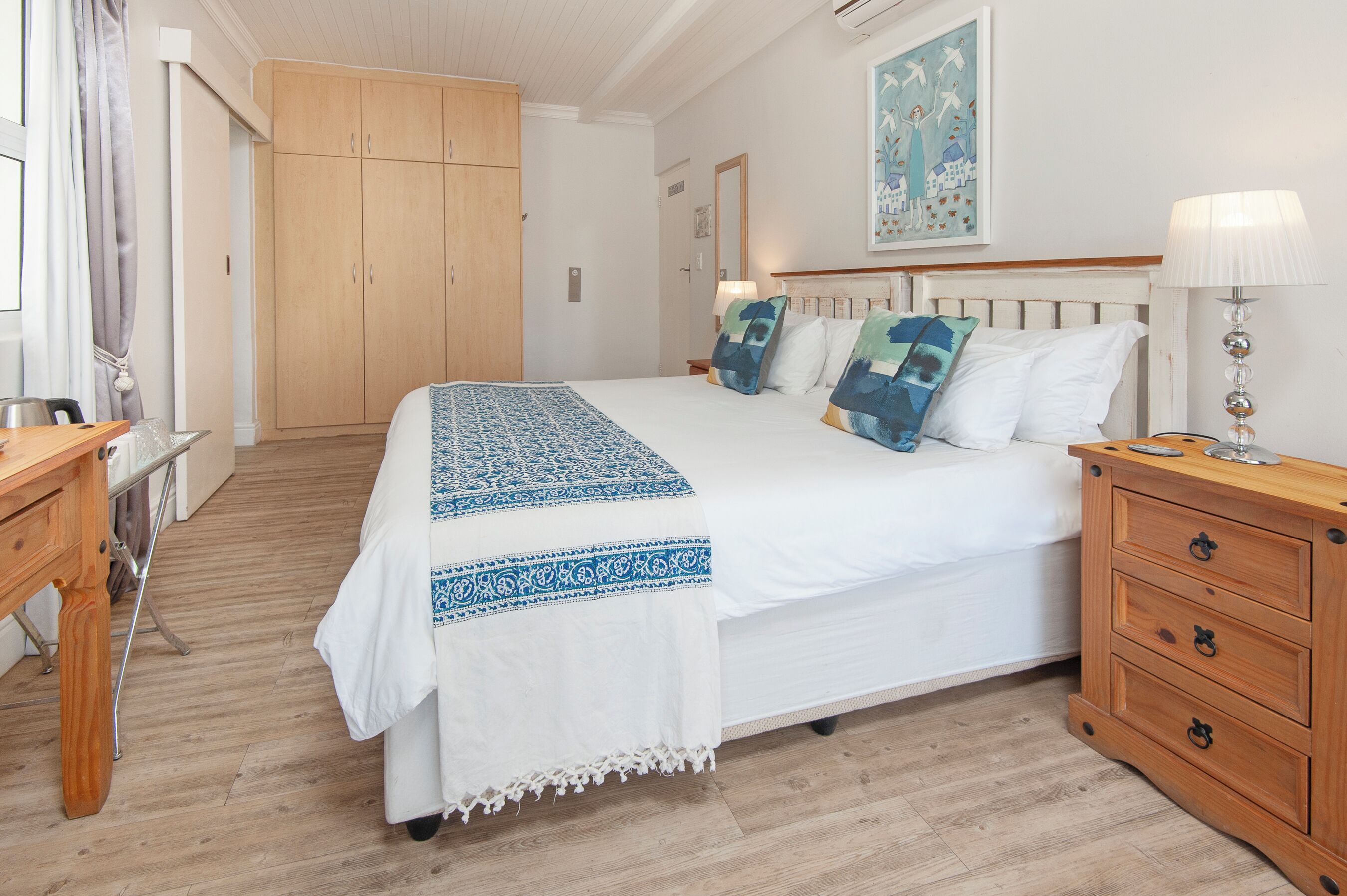 Une chambre avec un grand lit, une armoire en bois, des tables de chevet et un tableau au mur.
