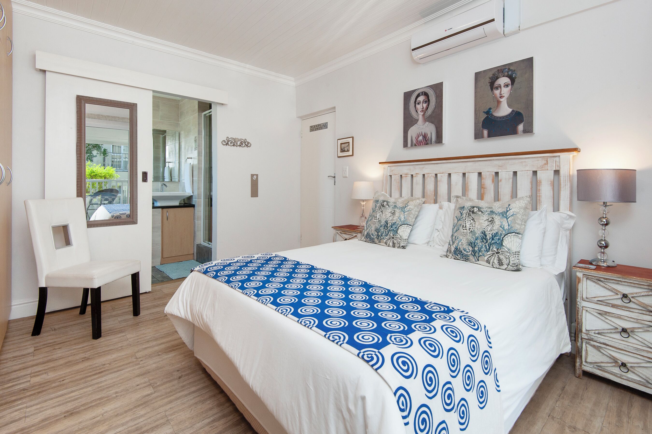 Un dormitorio con una cama grande, una silla, una mesita de noche con una lámpara y vistas al exterior.