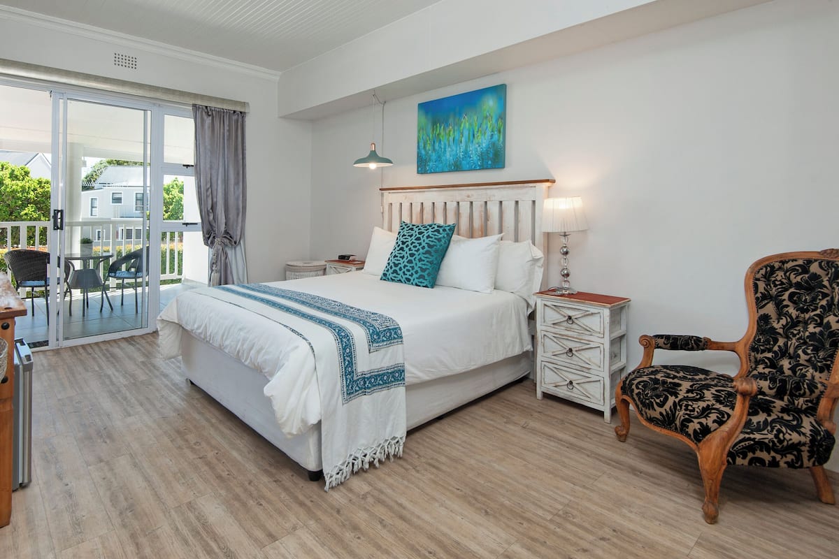 A bedroom with a bed, a chair, a nightstand, and a painting.