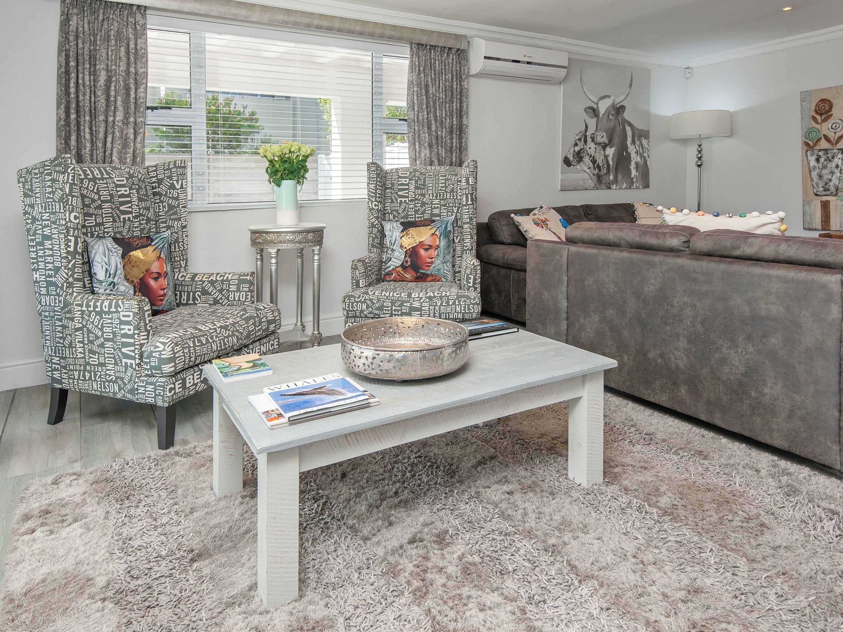 A living room with patterned armchairs, a grey sofa, a coffee table with magazines, and a decorative bowl.