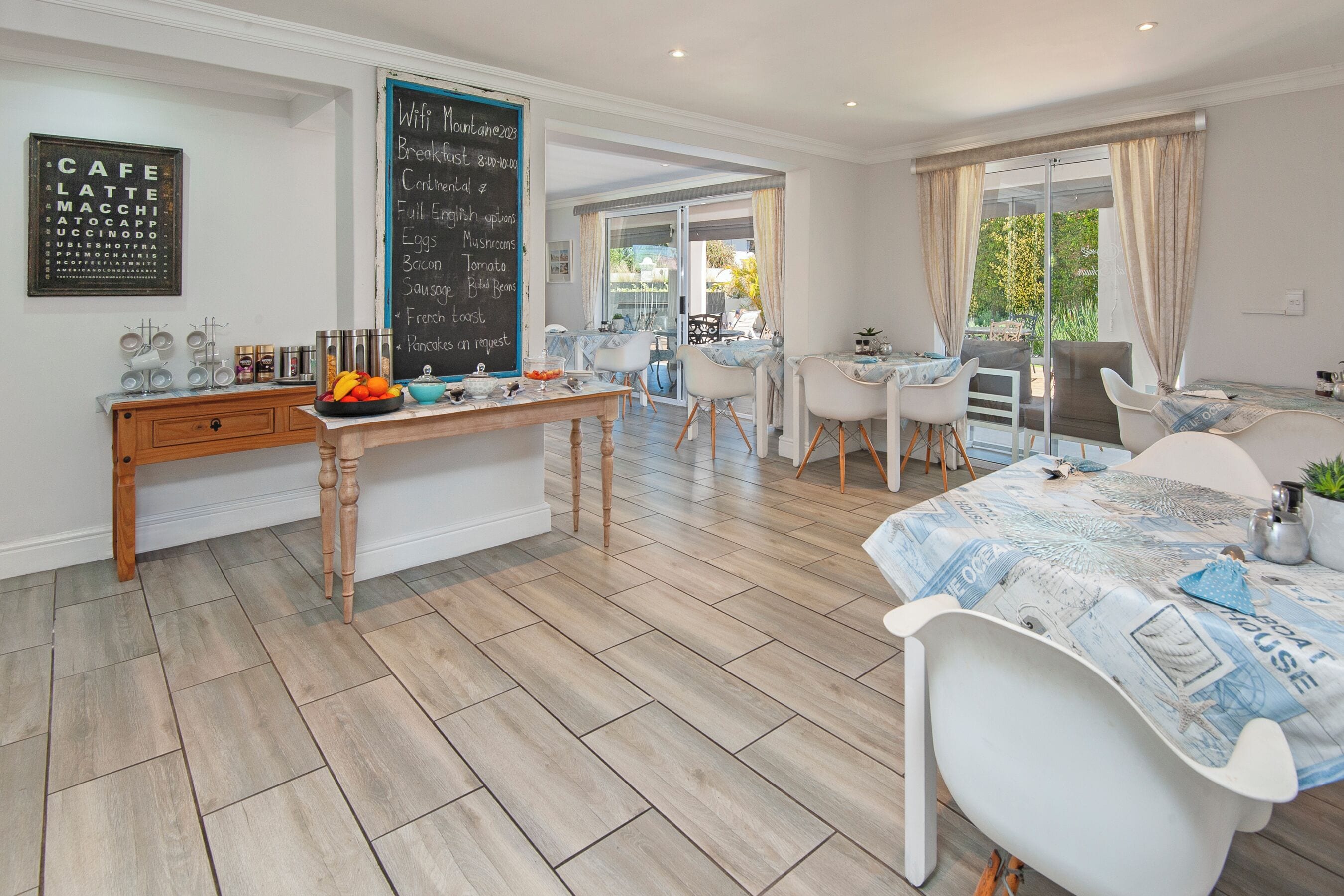 Una cocina moderna con un menú en pizarra, mobiliario de madera y un comedor con sillas blancas y una mesa.