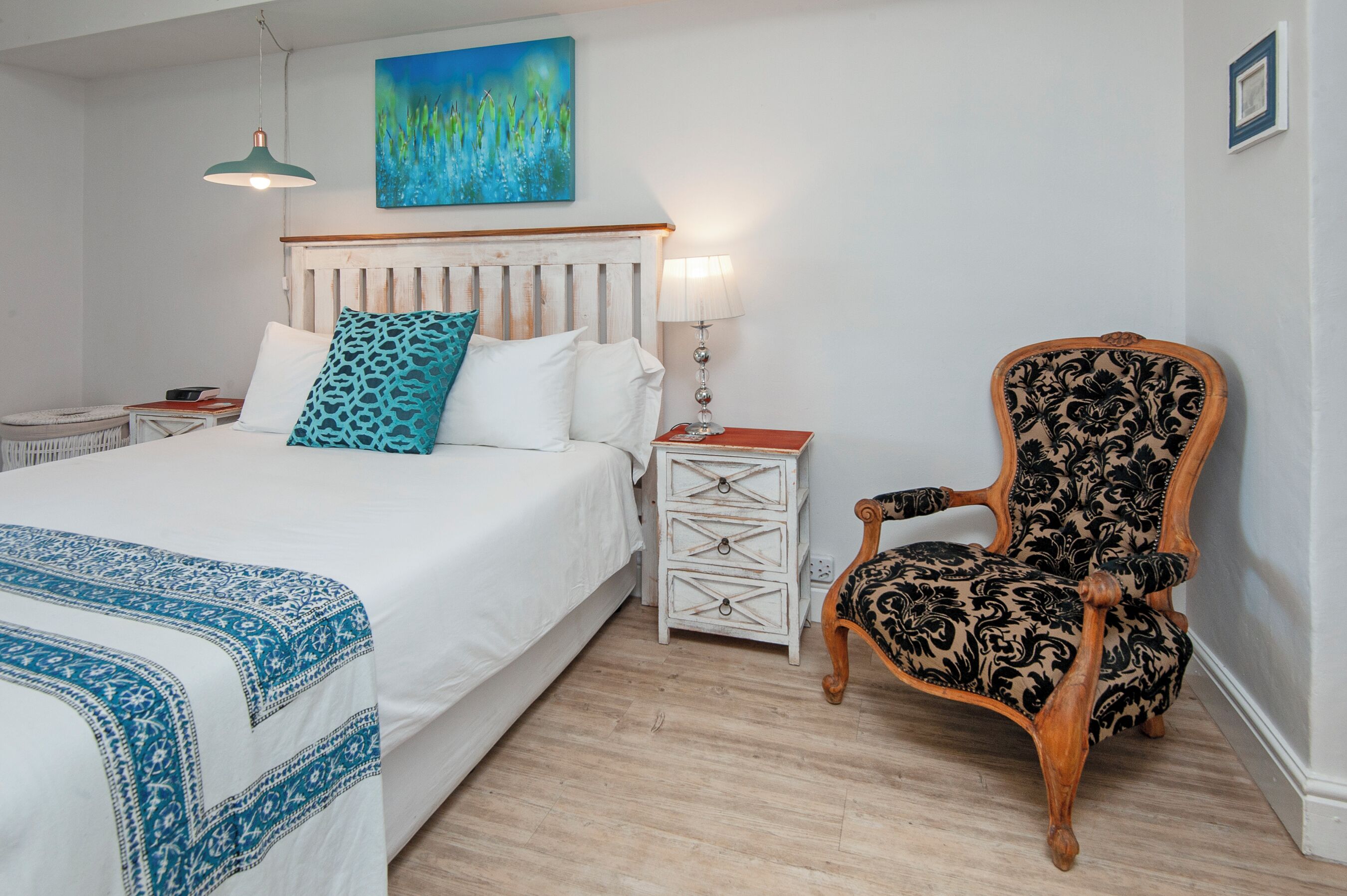 A bedroom with a bed, a nightstand, a chair, a lamp, and a painting on the wall.