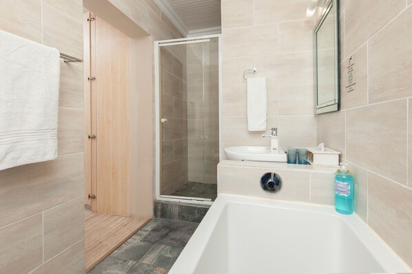Un baño moderno con ducha acristalada, lavamanos blanco y bañera.