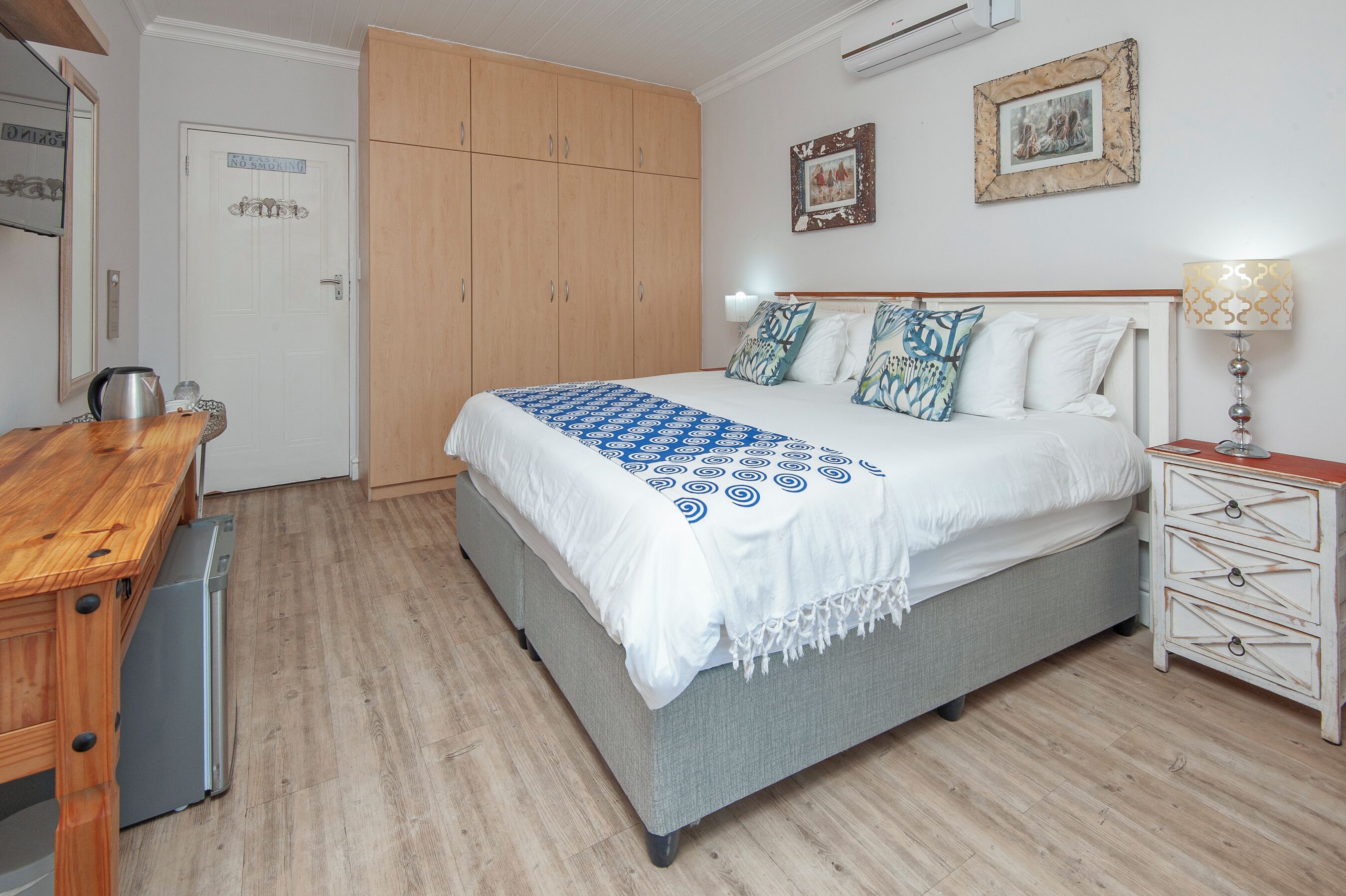 Een slaapkamer met een bed, nachtkastje, lamp, kast en een deur met een bordje.