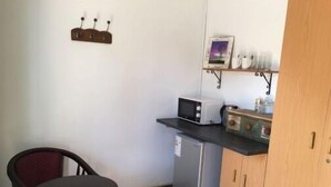 Cozinha compacta com geladeira, micro-ondas e uma pequena prateleira com xícaras e porta-retrato.