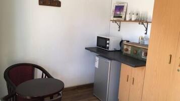 A compact kitchen with a refrigerator, microwave, and a small shelf with decorative items.