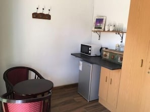 A compact kitchen with a refrigerator, microwave, and a small shelf with cups and a picture frame. - Cura Lodge (Bloemfontein)