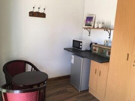 A compact kitchen with a refrigerator, microwave, and a small shelf with decorative items.