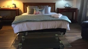 Cama bem arrumada com travesseiros, mesa de cabeceira com abajur e uma pequena mesa com copos.