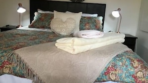 Uma cama bem arrumada com colcha estampada, travesseiros com texto e um relógio na parede.