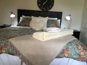 A neatly made bed with a patterned bedspread, pillows with text, and a clock on the wall. - Cura Lodge (Bloemfontein)