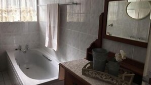 Casa de banho com banheira, toucador com espelho e janela com cortinas.