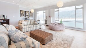 Un salon spacieux avec une grande fenêtre, un canapé à rayures, un pouf en osier et une vue sur la ville.