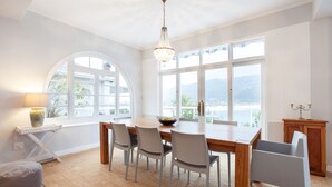 Un coin repas comprenant une table en bois, quatre chaises, un lustre et de grandes fenêtres donnant sur l’extérieur.
