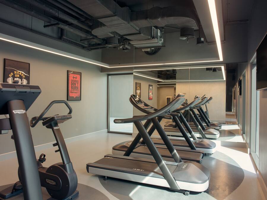 Un gimnasio con cintas de correr y elípticas, un espejo grande y carteles motivacionales.