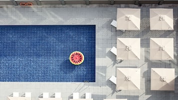 A rooftop pool with a blue mosaic floor, surrounded by white umbrellas and lounge chairs.