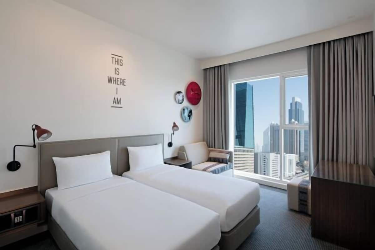 A hotel room with two beds, a city view, a desk, and a large window.