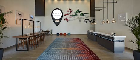 A hotel reception area with a long reception desk, a patterned rug, and a wall with a logo and abstract art.