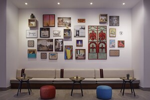 A gallery with various artworks on display, a seating area with a sofa and two tables, and a red and blue ottoman.