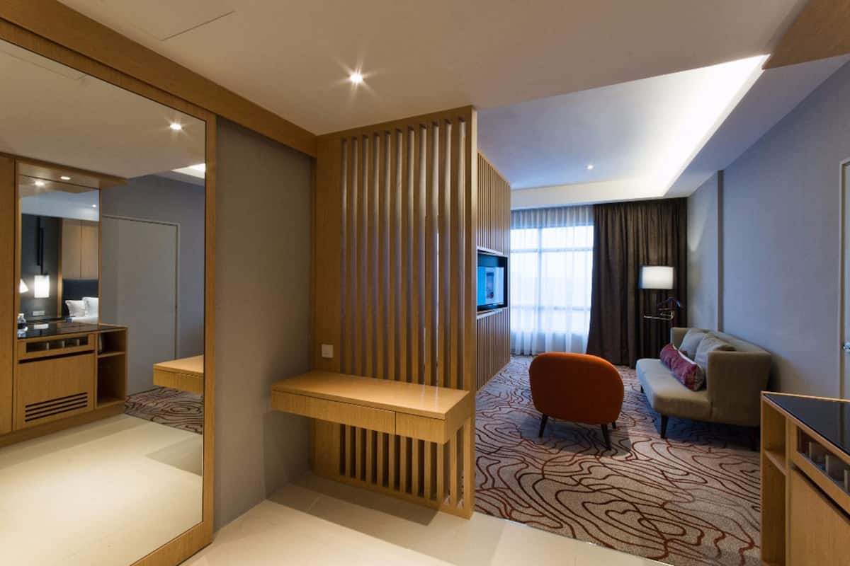 Une chambre d’hôtel avec un bureau en bois, un canapé, une télévision et un grand miroir.