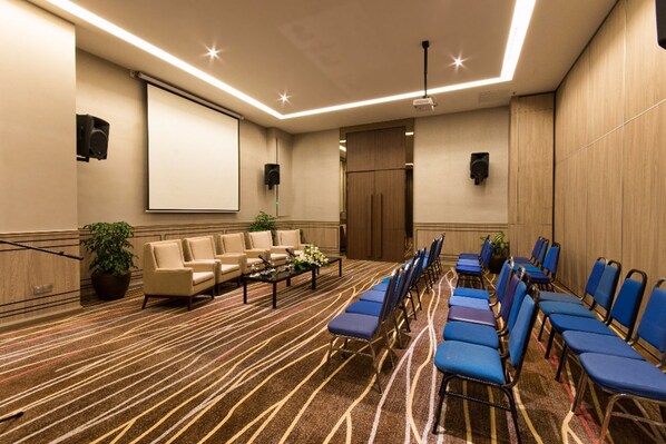A conference room with a long table, blue chairs, a projector screen, and a carpeted floor.