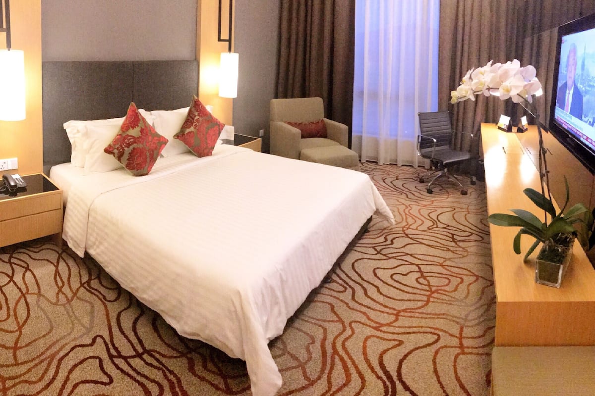 Une chambre d’hôtel avec un grand lit, deux tables de chevet, un bureau avec une télévision, une chaise, un canapé et une plante en pot.