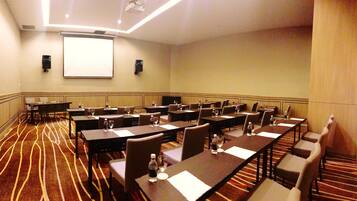 A conference room with multiple tables and chairs, equipped with water bottles and glasses, and a projector screen on the wall.