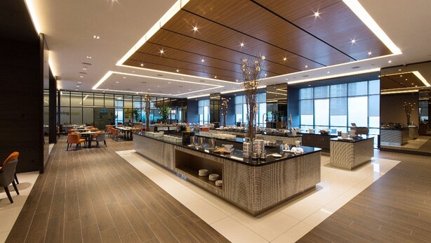 Een moderne hotellobby met een bar in het midden, zitgedeeltes en grote ramen die natuurlijk licht binnenlaten.