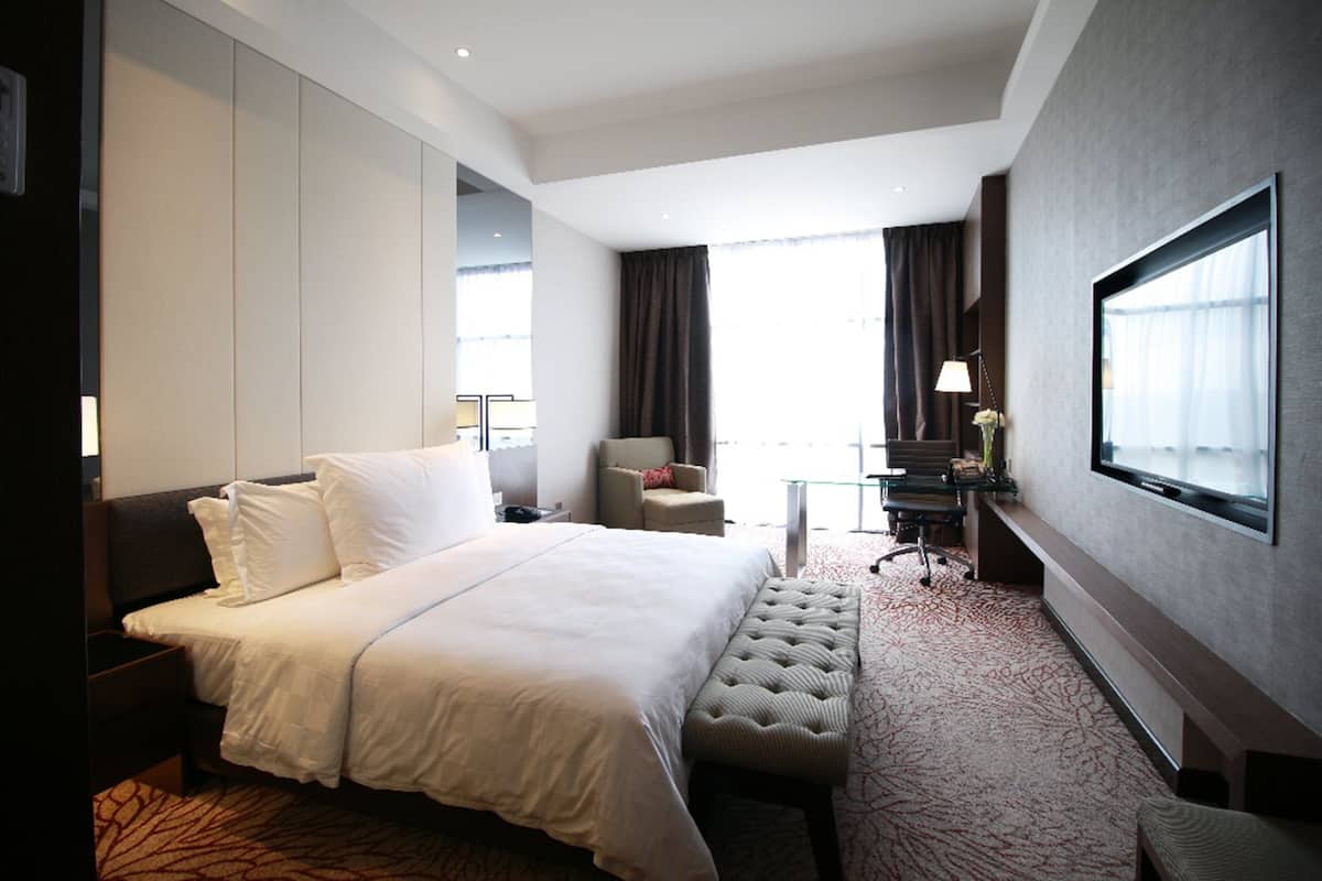 Une chambre d’hôtel avec un grand lit, un bureau avec une lampe, une chaise et un téléviseur fixé au mur.