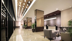 A modern hotel lobby with a marble floor, seating area, reception desk, and large mirrors. - Impiana Hotel Senai (Senai)